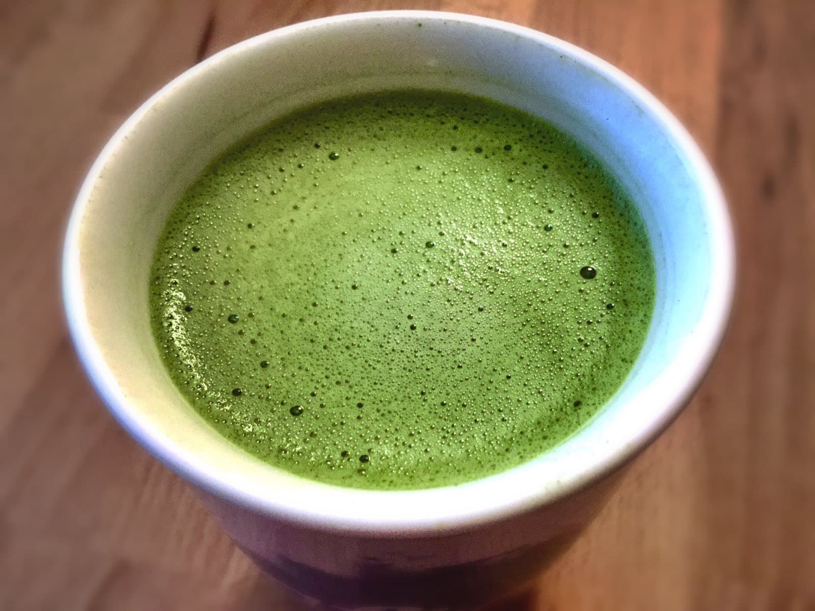 Ly matcha latte trong tách sứ đặt trên mặt gỗ, nhìn từ trên xuống