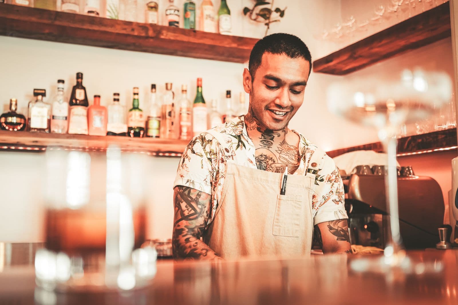 Bartender tươi cười chăm chút phục vụ khách sau quầy bar ấm áp — tinh thần hospitality và showmanship